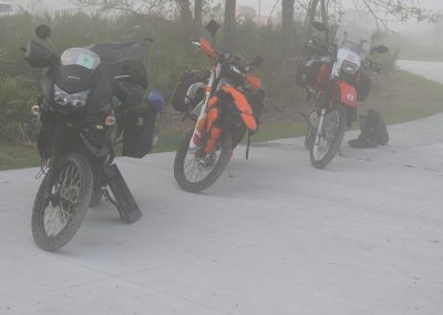 Three adventure motorcycles parked in morning fog