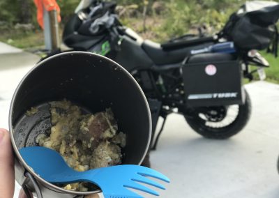 Camp meal in a backpacking pot next to a loaded adventure motorcycle